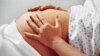Pregnant woman in hospital gown rubs her belly.