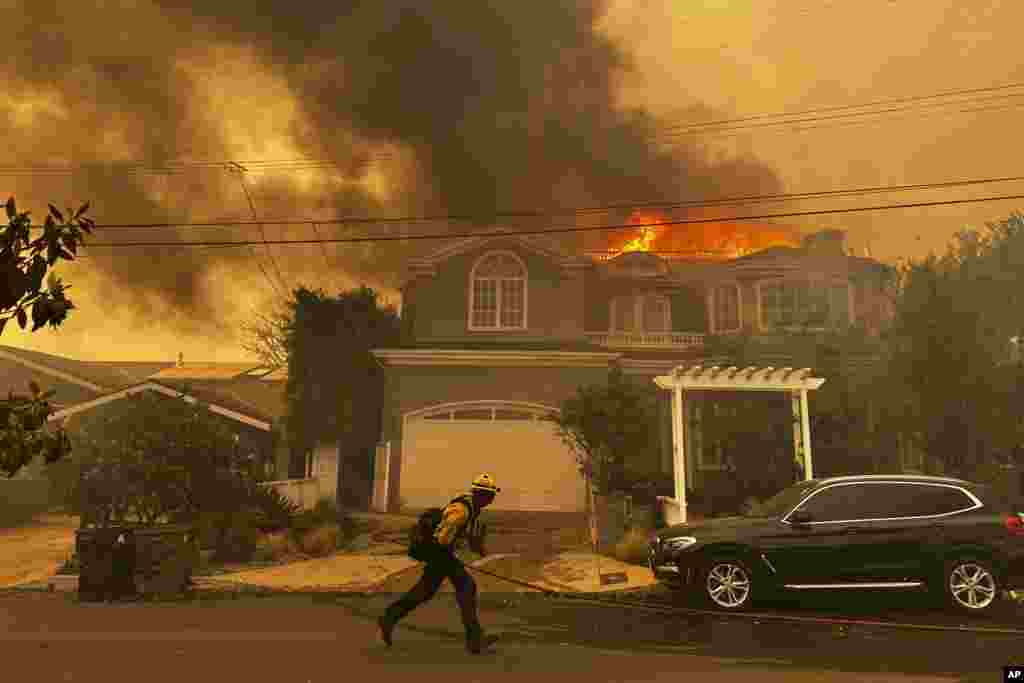 Uma residência arde enquanto um bombeiro combate o incêndio de Palisades, no bairro de Pacific Palisades, em Los Angeles, a 7 de janeiro de 2025.