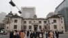 People wearing face masks walk by the headquarters of the Bank of Korea in Seoul, South Korea, March 4, 2021. South Korea's central bank says the country's economy shrank for the first time in 22 years in 2020. 