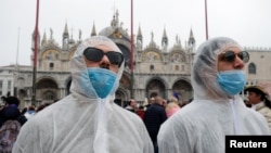 FILE - Tourists wear protective face masks at Venice Carnival, which the last two days of, as well as Sunday night's festivities, have been cancelled because of an outbreak of coronavirus, in Venice, Italy, Feb. 23, 2020. 
