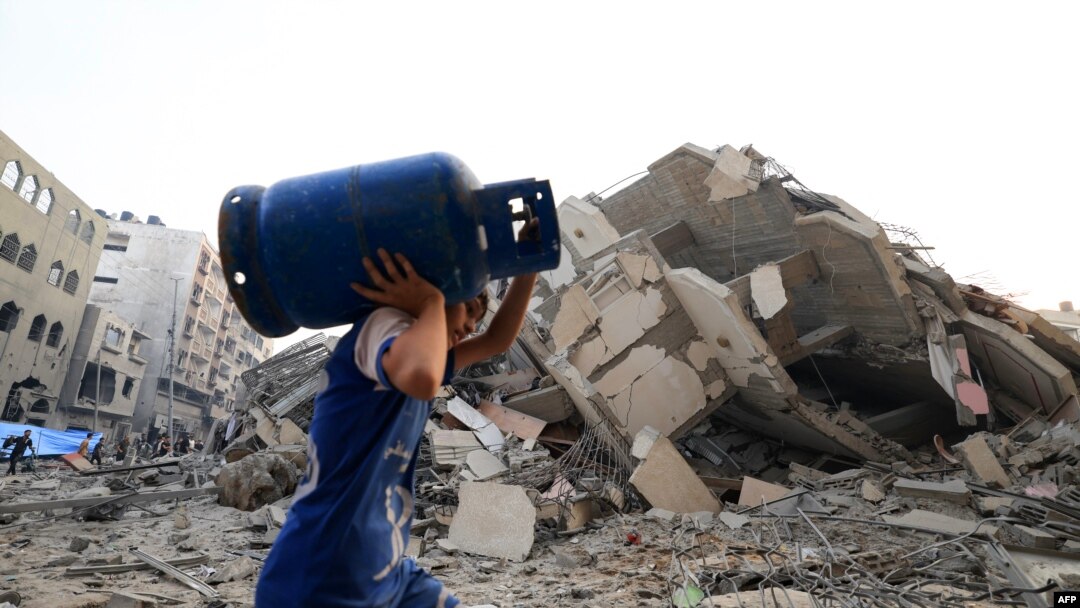 A boy carries a gaz canister as he walks in front of a building that collapse during an Israeli air strike in Gaza City early on October 8, 2023.