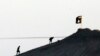 FILE - In this image shot with an extreme telephoto lens and through haze from the outskirts of Suruc at the Turkey-Syria border, militants with the Islamic State group are seen after placing their group's flag on a hilltop.
