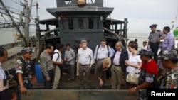 FILE - Myanmar government officials and U.N. officials stand on a boat used for human trafficking at a jetty outside Sittwe, Myanmar.