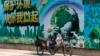 A migrant worker listens to radio on his tricycle cart parked next to a billboard promoting environment protection with the slogan "Environment protection starts from you and me" on display at the Central Business District of Beijing, June 5, 2017. 