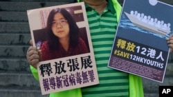 FILE - A pro-democracy activist holds placards, with the one on the left picturing Chinese citizen journalist Zhang Zhan, outside the Chinese central government's liaison office, in Hong Kong, Dec. 28, 2020.