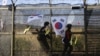 Tentara Korea Selatan berjaga-jaga di sekitar Paviliun Imjingak, mengibarkan bendera dan pita nasional sambil mengekspresikan harapan akan reunifikasi Korea. Lokasi ini, berada di dekat Panmunjom, zona demiliterisasi yang memisahkan kedua Korea sejak Perang Korea. 