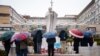 Pessoas rezam debaixo de chuva junto à estátua de João Paulo II no Hospital Universitário Gemelli, onde o Papa Francisco está hospitalizado com pneumonia, em Roma, a 1 de março de 2025.