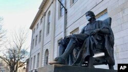 哈佛大学学生陆续搬离宿舍。图为哈佛大学一座地标雕塑，疫情之下有人为它也戴上了口罩。（2020年3月14日）